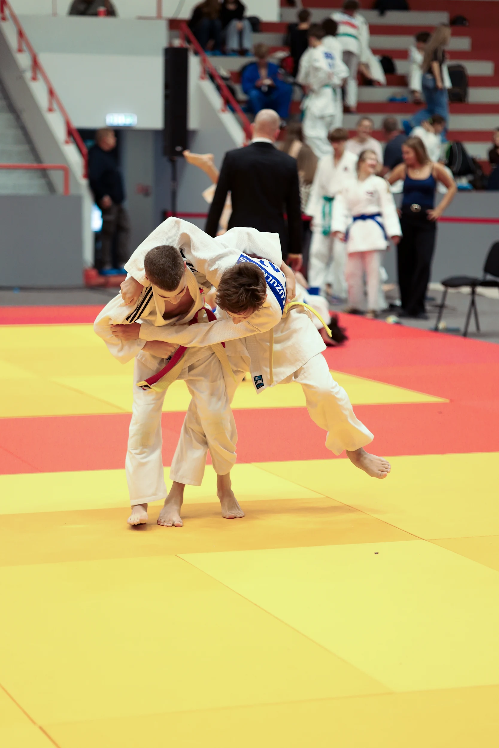 Metiena brīdis bērnu džudo cīņā sacensībās; fonā redzami tatami un tribīnes